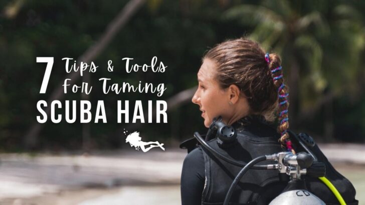 A scuba diver walks away from the camera on a white, sandy beach. Her long hair is tied up with a blue and pink hair tie. Overlaid white text reads 