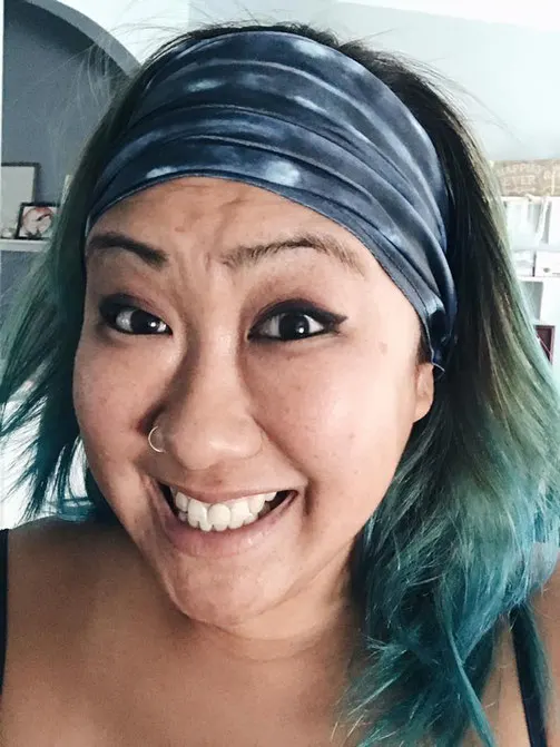 Woman smiles happily at the camera with her blue hair pulled back using a whale shark print buff