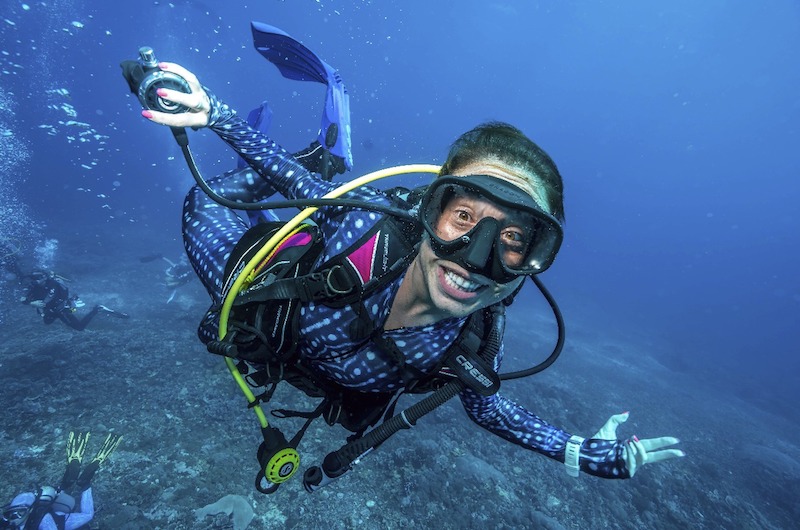 Woman scuba diving smiling at the camera holding her regulator to the side