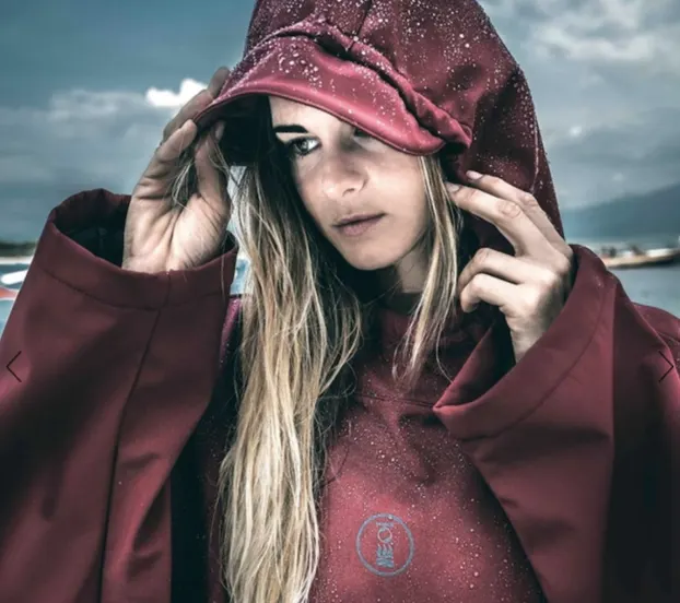 Woman wearing a burgundy Fourth Element storm poncho to shield from the rain