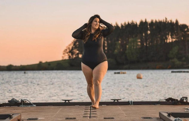 Woman stands on a dock at dusk in a long sleeved black plus size swimsuit