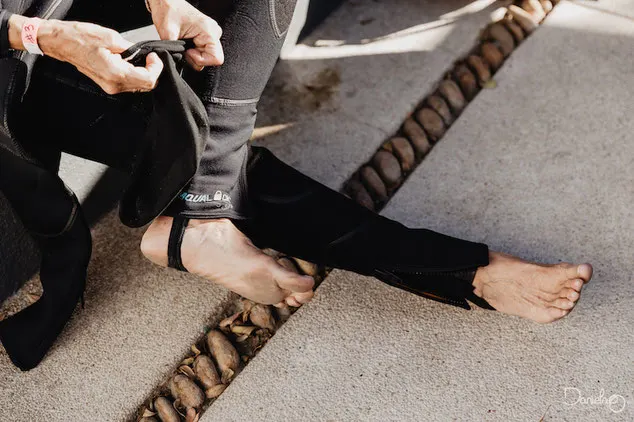 Scuba diver sitting on the floor of a boat pulling on neoprene socks