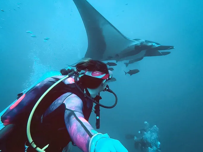 Underwater GoPro selfie of a woman scuba diving with manta ray