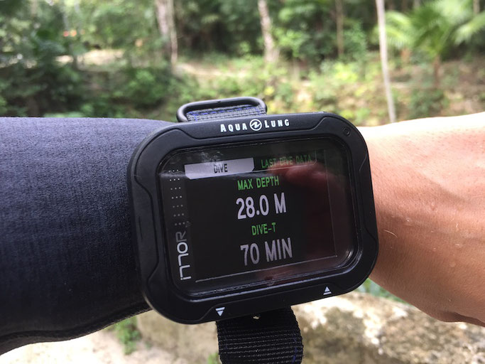 Close up of a forearm with a large rectangular dive computer on the wrist, displaying dive details