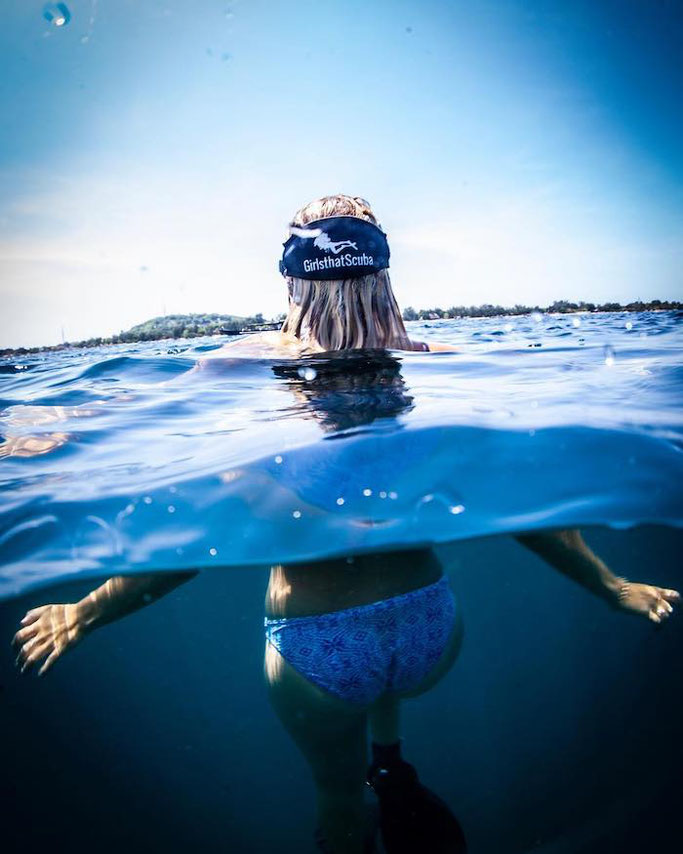 The back of a freediver's head, floating at the surface and wearing a blue Girls that Scuba mask strap