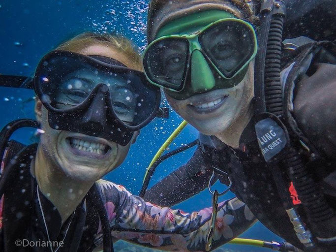 Two scuba divers smiling underwater in a black scuba mask and a green scuba mask 