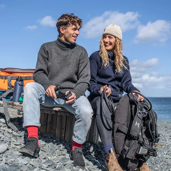 A man and woman smile at each other preparing for a scuba dive, wearing sustainable jumpers, hats and socks by Fourth Element