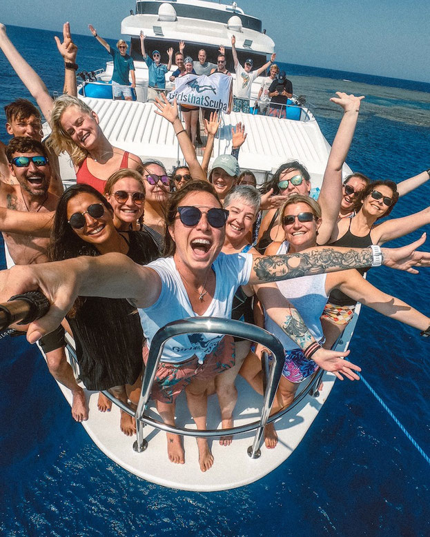 A group of scuba divers cheering standing on the front of a diving liveaboard on a Girls that Scuba group trip