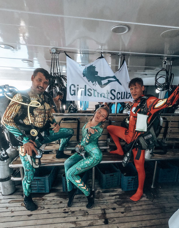 Group of scuba divers dressed in brightly coloured lycra superhero suits on the deck of a diving liveaboard.