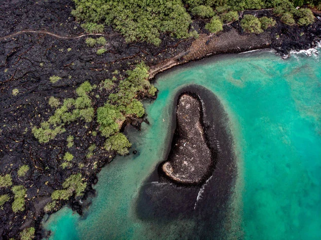 Aerial drone image of blue coastline against volcanic black beach in Kailua-Kona Hawaii