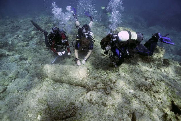 Three scuba divers underwater during a marine archaeological expedition looking at a column near Cyprus