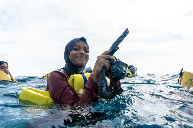 A girl smiles at the camera whilst floating at the surface, holding a snorkel and mask