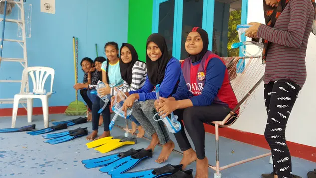 A group of girls smile at the camera with snorkelling fins laid out in front of them
