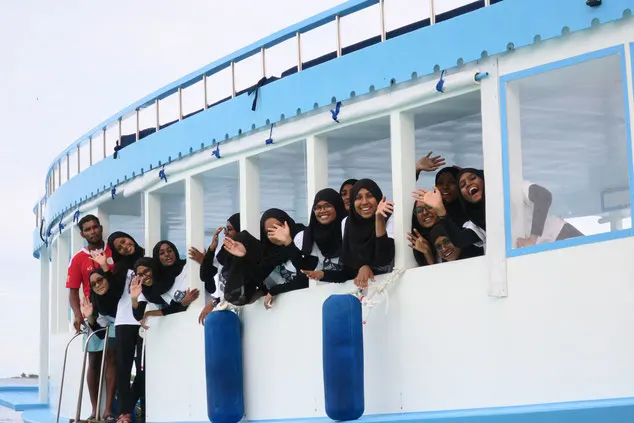 A group of young women smile and wave from a boat