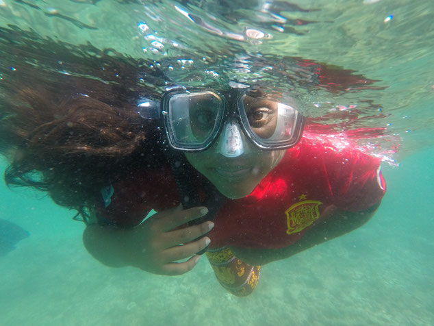 A young girl with flowing dark hair swims towards the camera under the surface wearing a snorkel mask