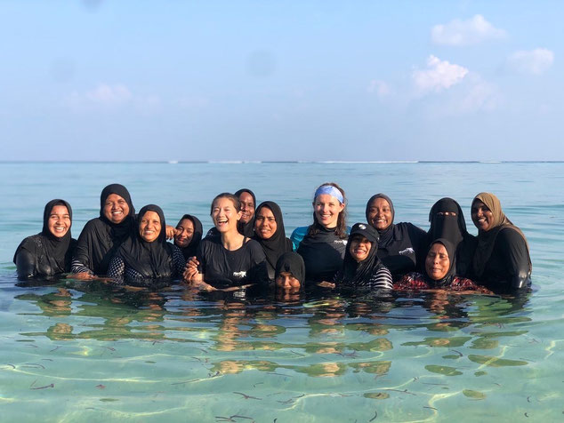 Women smiling at the camera whilst standing in clear, shallow water