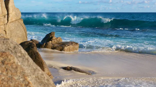 Beach on La Digue island, Seychelles, with large boulders in the foreground and blue ocean in the background with medium size waves