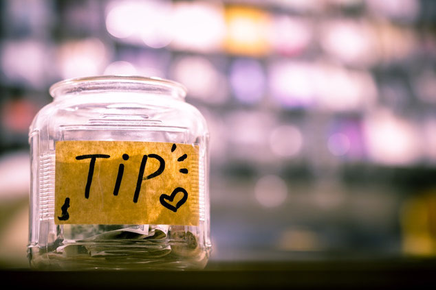 Glass jar filled with cash with yellow label reading "tip" against a blurred background