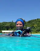 Woman scuba diver, Rose, looks into the camera at the surface of bright blue water