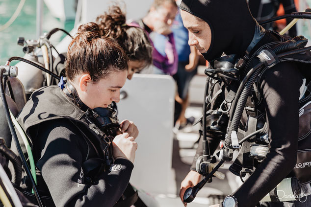 Scuba instructor helping a student with equipment on a boat