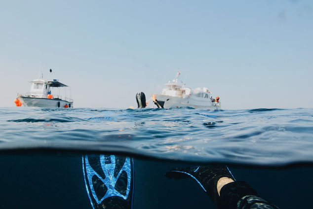 Split underwater shot showing scuba fins underwater and a large dive boat in the background