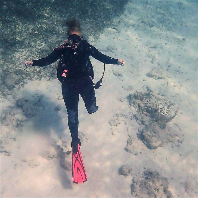 Amber scuba diving, she is wearing black scuba equipment and one pink fin on her right leg. 