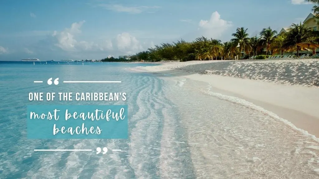 Clear waters lap onto the bright white sands of Seven Mile Beach, bordered by idyllic yellow buildings and bright green palm trees