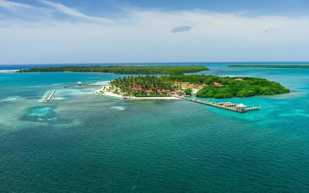 Drone image of a lush green island with bright white beaches and small red-roofed buildings, in turquoise waters