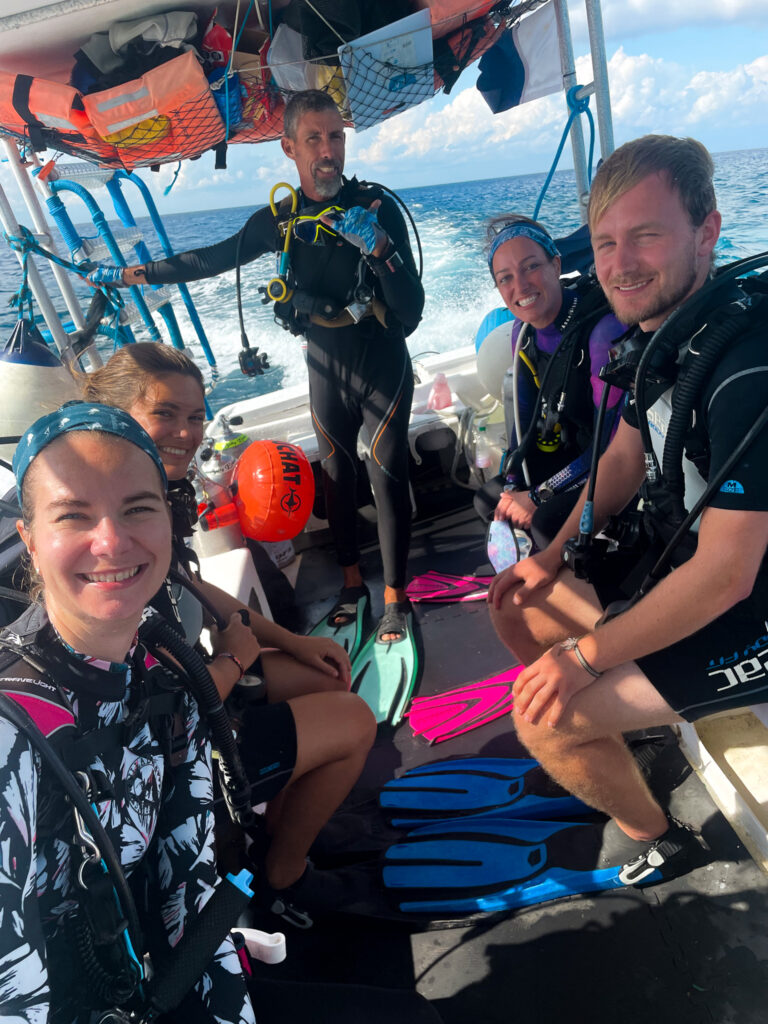 Group of scuba divers sat on the boat in their equipment smiling at the camera