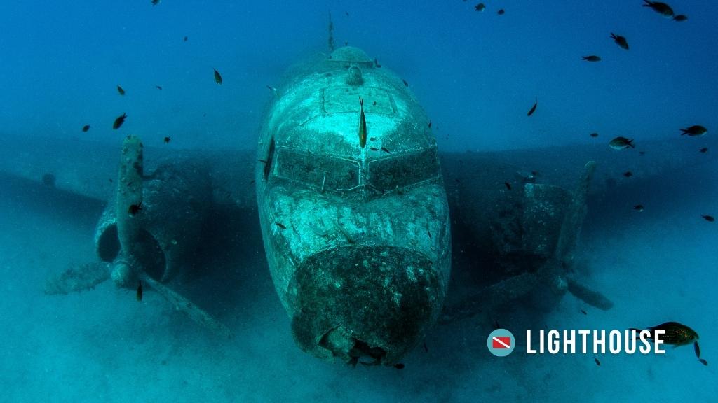 A plane submerged underwater in Kas, Turkey, at Lighthouse dive site. The plane is covered in algae and surrounded by small fish.