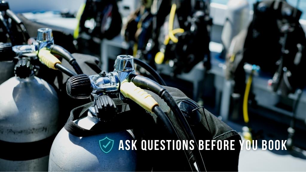Scuba cylinders with dive gear set up on a sunny dive deck. Overlaid white text reads "ask questions before you book".