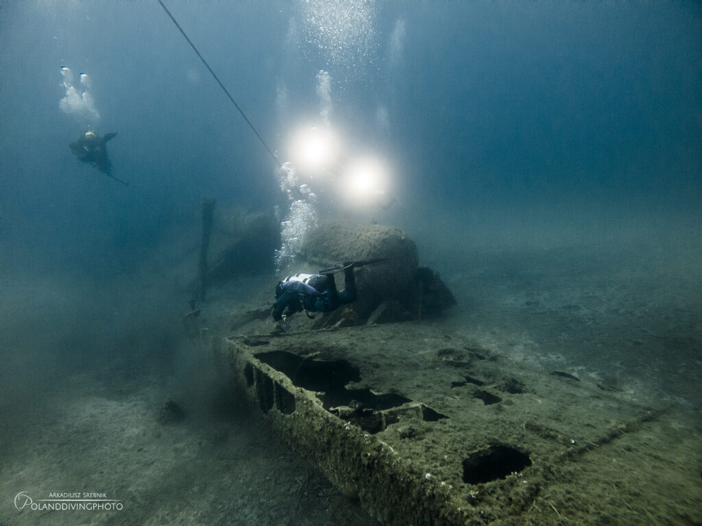 Scuba diving in Gallipoli around the HMS Louis wreck. A diver swims away from the camera above the wreck, and more divers' lights can be seen in the background. 