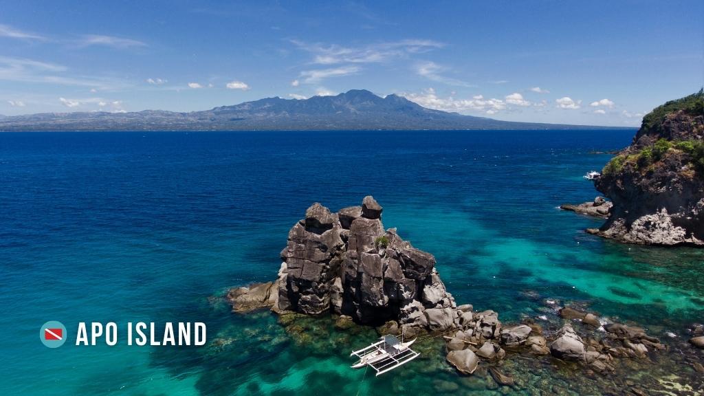 Aerial view of a small rocky outcrop in vibrant blue water, in Apo Island, Philippines. 