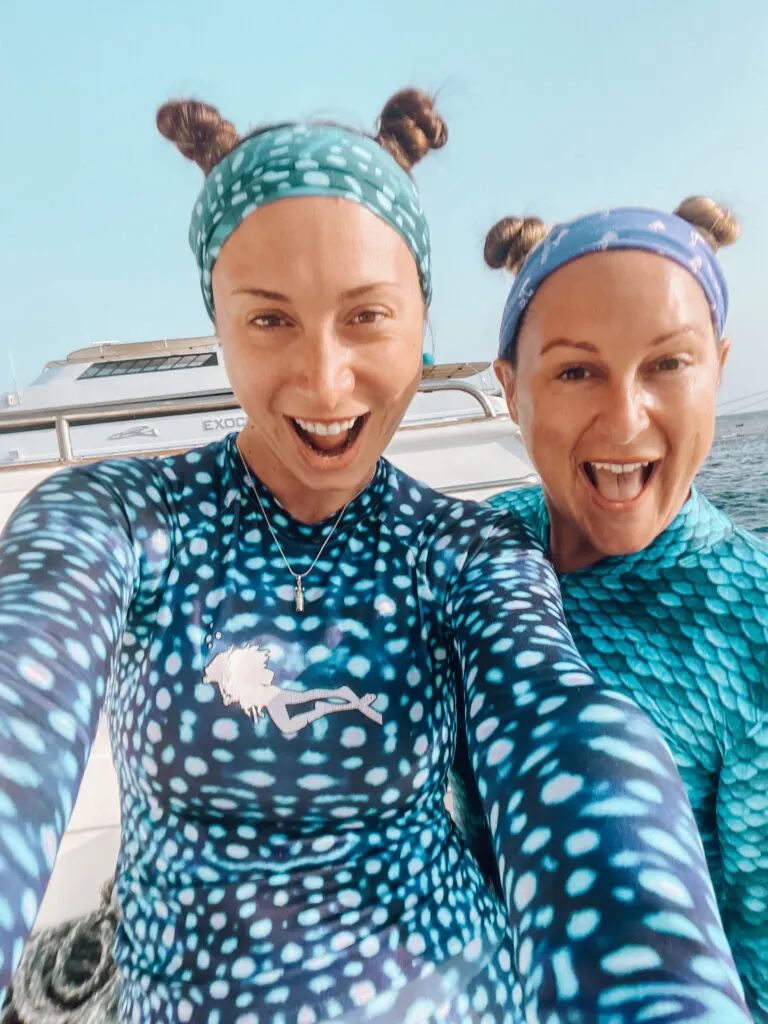 Two women divers smile at the camera wearing scuba headbands and with their hair in two small "space" buns on the top of their heads.