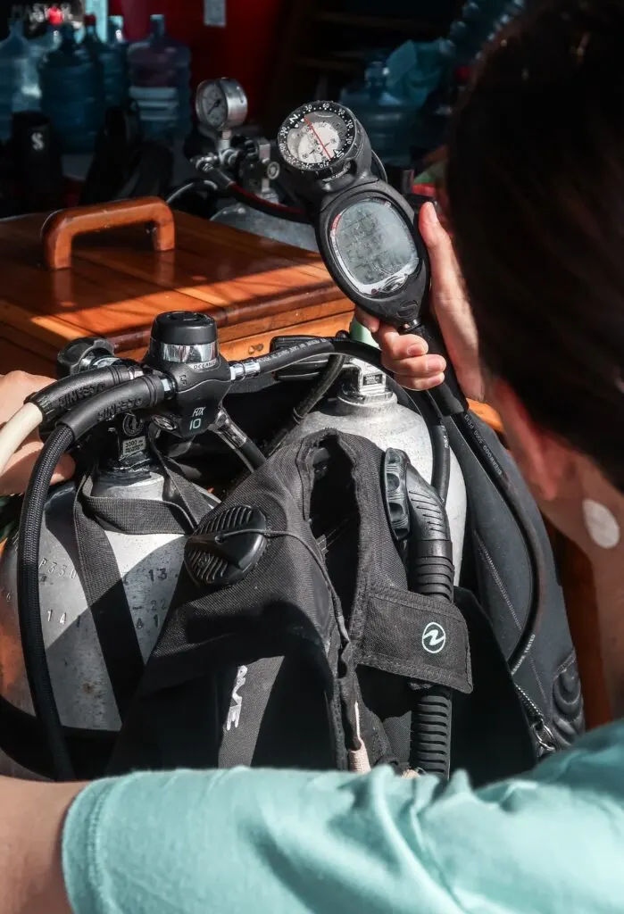 A woman diver checks the gauge of her equipment whilst opening the cylinder valve. 
