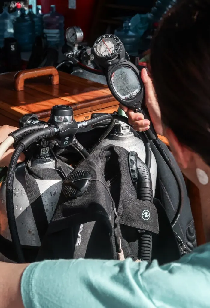 A woman diver checks the gauge of her equipment whilst opening the cylinder valve.
