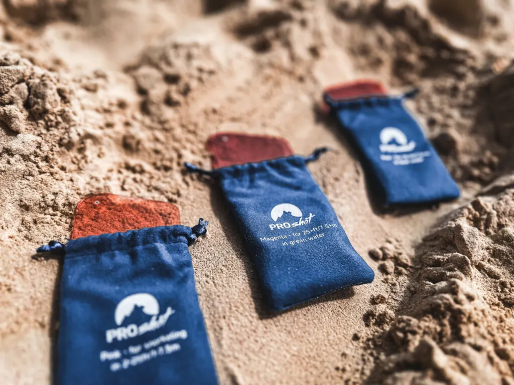 Three translucent red pieces of plastic sit on the sand, peeking out of small blue bags. 