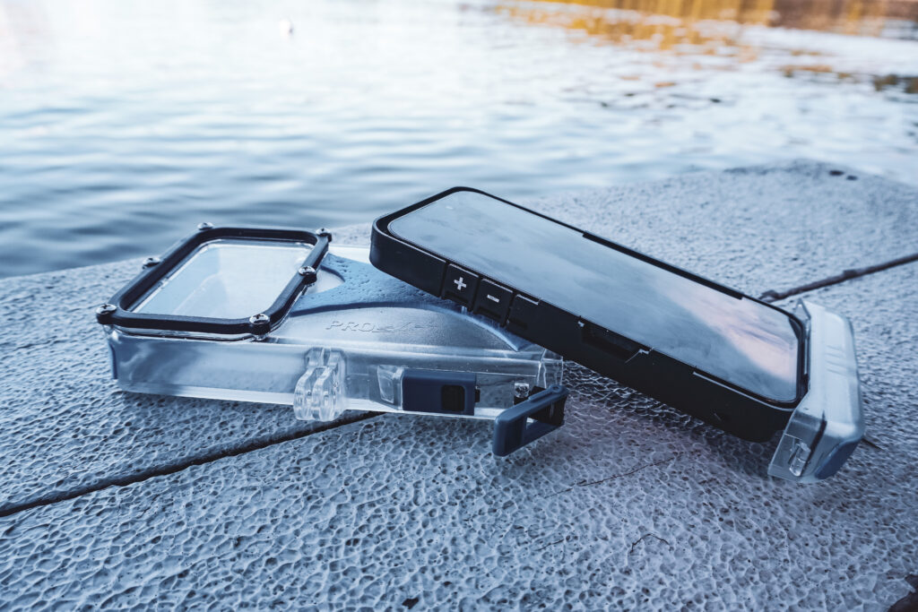 The ProShot Dive Case sits on a surface with water in the background. The case is open, with an iPhone resting on top.