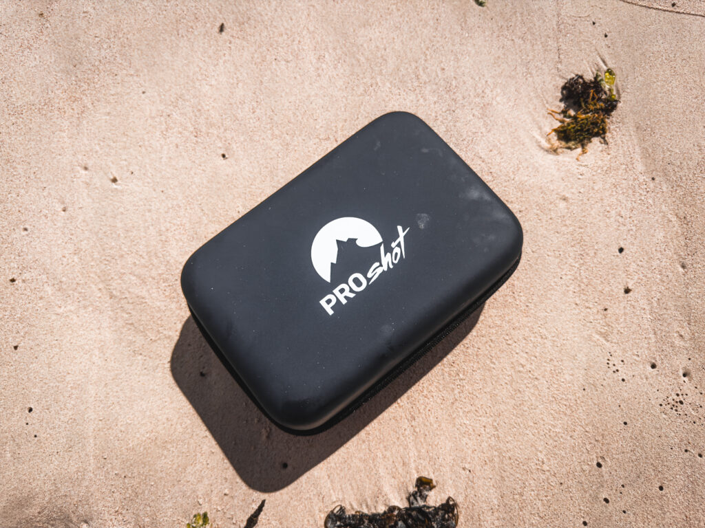 A black case with white writing reading "ProShot" and a white logo sitting on a sandy beach.